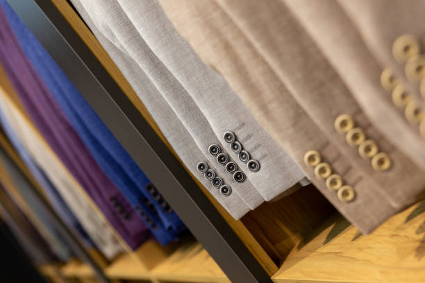 A row of men's suits, jackets hanging on a rack for display. Elegant man suit jackets hanging in a row with close up of sleeve and buttons.