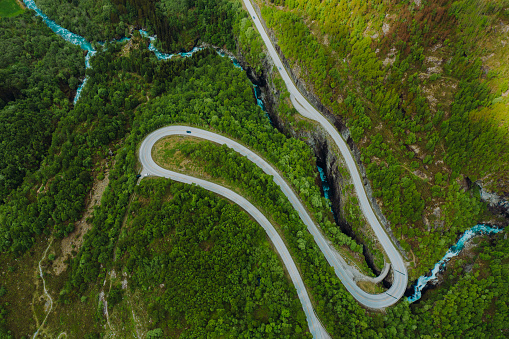 High-angle drone photo a vehicle driving the picturesque curve mountain pass surrounded by wonderful green mountains, small town and the glacier in Jostedalbreen National Park, Stryn, Western Norway