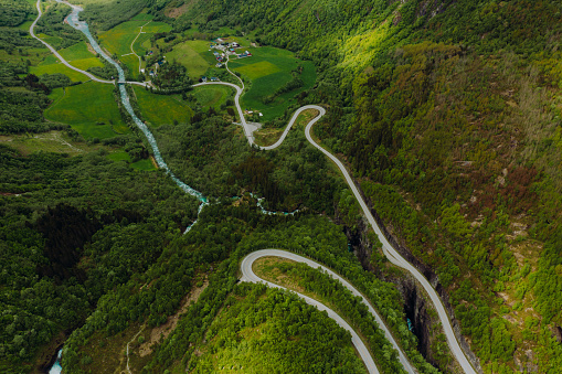 High-angle drone photo a vehicle driving the picturesque curve mountain pass surrounded by wonderful green mountains, small town and the glacier in Jostedalbreen National Park, Stryn, Western Norway