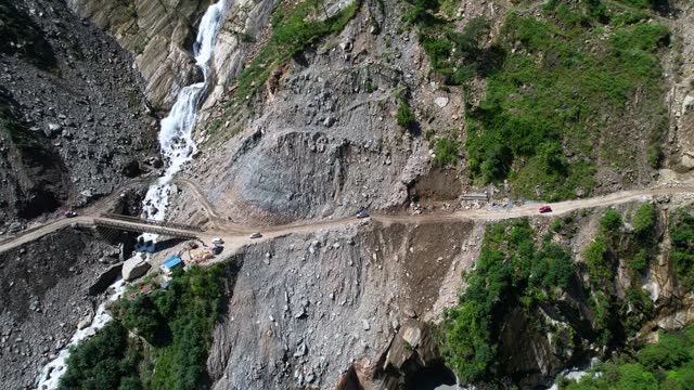 Rupse Falls And Off-road SUV Cars Drive on Steep Slope Mountain Dirt Road Crossing Bridge Over Waterfall in Central Nepal - Aerial Dolly