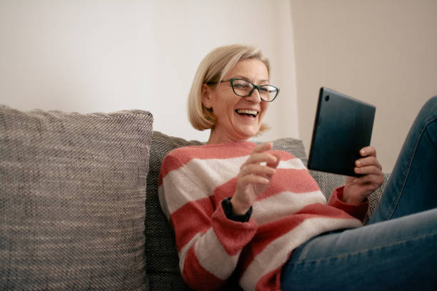 istock mature blonde woman sitting on sofa and using tablet for video call 2025875853
