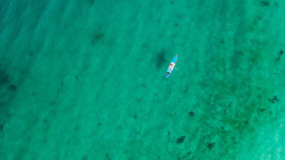 Drone high-angle photo of female on blue paddle board crossing the turquoise ocean during sunny summer day at the western fjords of Norway, Scandinavia