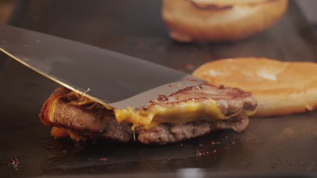 Cooking American fat smash burger with cheese slice on top on grill close-up. Beef or pork cutlet smashing by burger press. The chef in kitchen of the restaurant making cutlets for burgers - smash