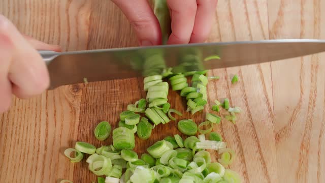 The chef in the kitchen prepares a healthy salad, chops leeks on a wooden board. Close-up, side view, macro