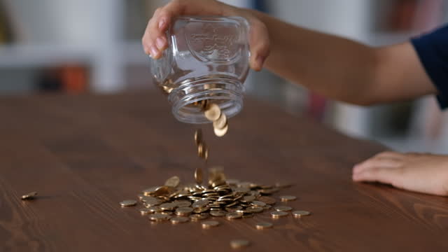 little boy is pouring coins on the table from the jar