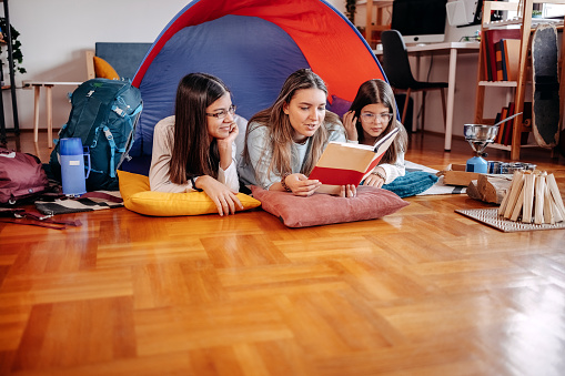 Babysitter playing with kids in open tent in living room reading a book