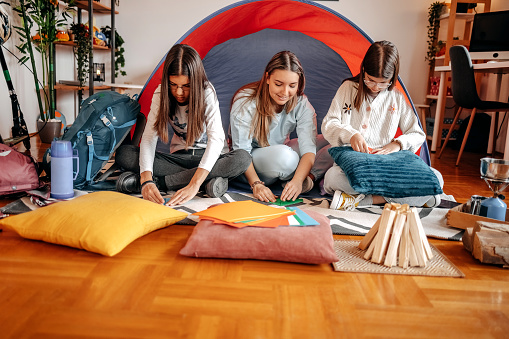 Babysitter playing with kids in front of tent in living room using paper to make origami