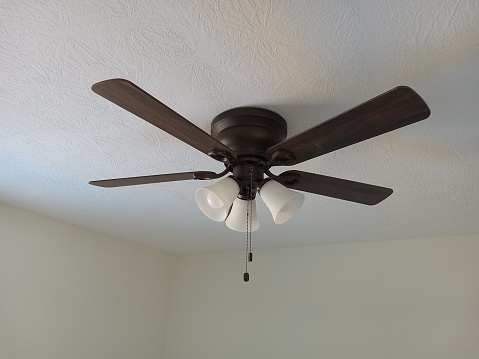 A ceiling fan that is turned off with its shadow on the ceiling.