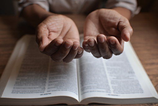 close up on the hands of an unrecognizable woman reading the bible and praying. Concept of religiosity and mystery