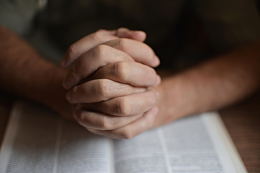 close up on the hands of an unrecognizable man reading the bible and praying. Concept of religiosity and mystery