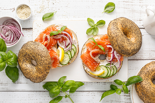 Salmon sandwiches with bagel, salted fish, fresh cucmber, onion and basil on white background, top view. Healthy breakfast with salmon toasts