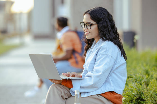 istock Young Latin female student using laptop on the bench on campus 2026162571