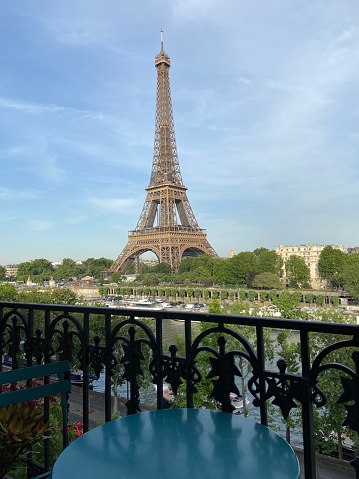 View of the Eiffel Tower from an apartment balcony with an ornate railing and a small, green metal table and chair in the 16th arrondissement in Paris, France at dusk