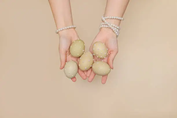 Photo of female hands in pearl bracelets hold painted Easter eggs decorated with beads