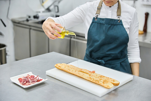 Female cook preparing sandwich in bakery kitchen.