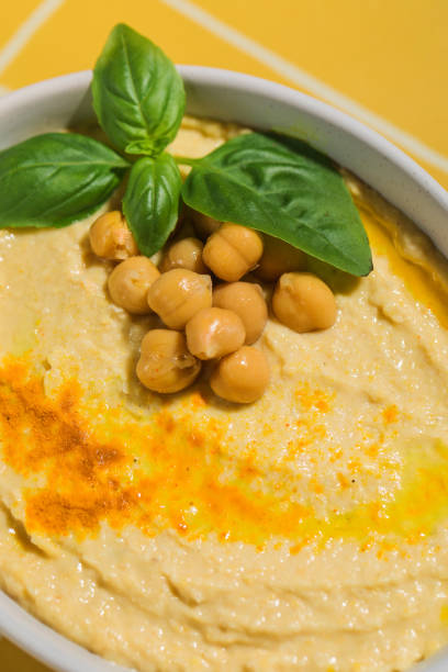 A dish of hummus topped with chickpeas and basil served on a yellow tile table