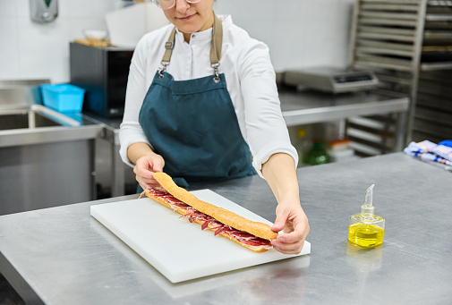 Female cook making baguette sandwich in kitchen