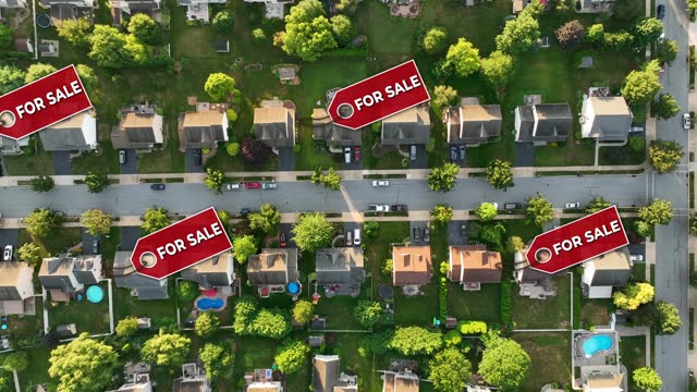 Neighborhood with multiple For Sale signs over homes. Top down aerial truck shot above modern American housing development. Animated tags appear on houses. Real estate theme.
