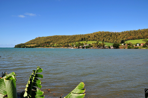 Petit Sable, Grand Port District, Mauritius: north shore of the Pointe du Diable headland (Devil's Point!), with the Petit Sable hamlet, seen from across the bay, with banana tree leaves on the left.