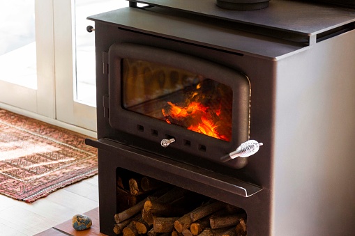 Close-up view of a metal fireplace stove burning brightly in a cozy living room.