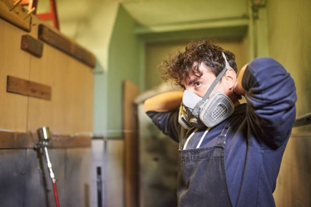 Man removing a protective respirator mask as he finishes his spray painting job Portrait of a young hispanic worker removing a protective respirator mask as he finishes his spray painting job in his workshop. Real people at work. workplace absence stock pictures, royalty-free photos & images