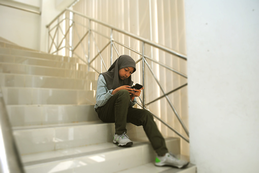 Teenage Asian girl using smartphone on the staircase.