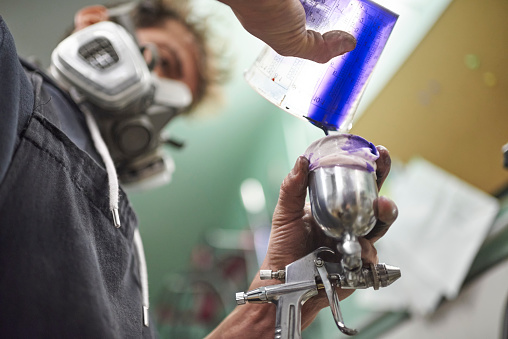 Man pouring paint into a spray paint gun tank in his workshop to paint a bike with airbrush. Low angle view composition with copy space.