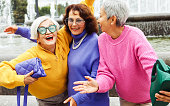 Three happy cheerful pensioner girlfriends in bright sweaters and sunglasses walk together