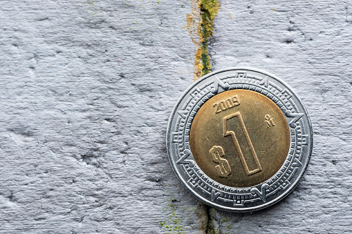 Macro photo of one peso Mexican coin over a grey concrete surface.