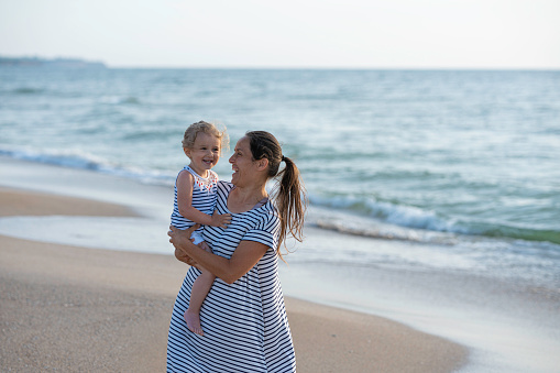 Mom with little girl playing on the beach at sunset.