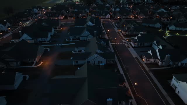 Aerial truck shot of dark neighborhood at night. Development with town lights in background. High view at dusk with car headlights.