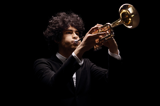 Young man in a black suit playing a trumpet isolated on black background