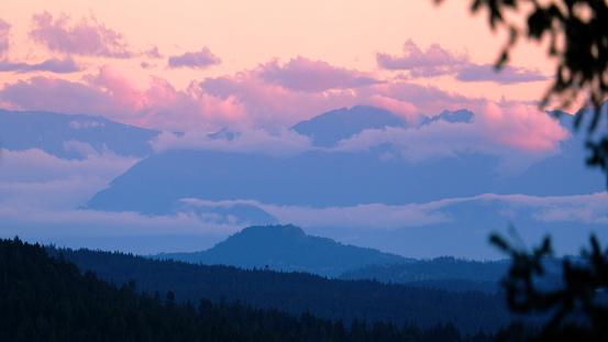 Layered hills view towards pink clouds over the Olympic peninsula in Washington State USA.