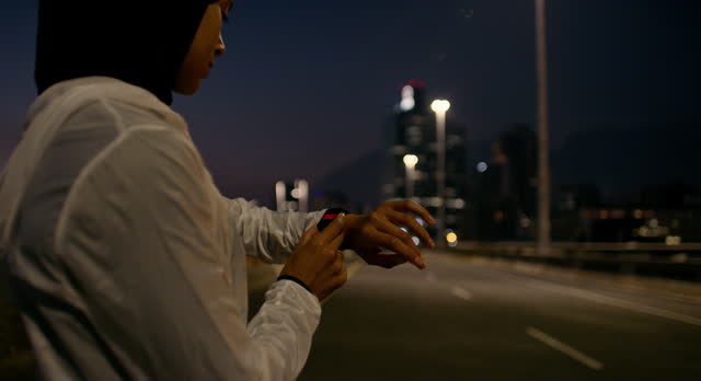 Muslim woman, fitness and checking watch at night in city for performance, monitoring or tracking. Active athlete, female person or runner with wristwatch for cardio, time or start in an urban town