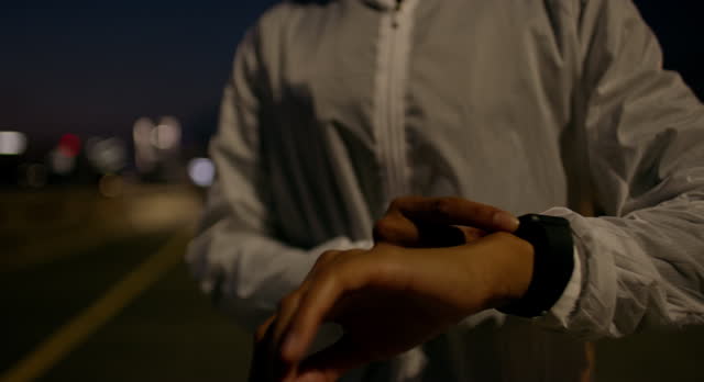 Person, hands and checking watch at night for fitness, performance or tracking in the city. Closeup of active athlete or runner with wristwatch for monitoring cardio, time or start in an urban town