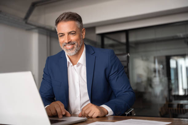 istock Smiling 40s mature Latin business man ceo trader using computer, typing, working in modern office, doing online data market analysis, thinking planning tech strategy looking at laptop with copy space. 2026509976