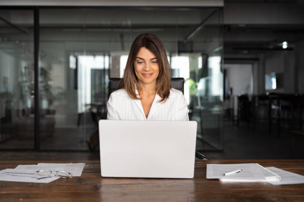 istock 40s mid age European business woman CEO using laptop application for work sitting at table workspace in office. Smiling Latin Hispanic mature adult professional businesswoman using pc digital computer 2026510532