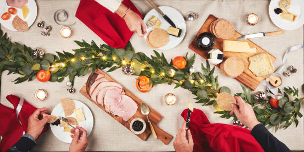 肉、豚肉、家族のお祝いのためのクリスマスの飾り付けでテーブルにいる人々の手。スナック、ハイアングル、クラッカー、ハム、チーズの盛り合わせで、お祝いのディナーパーティーの前�
