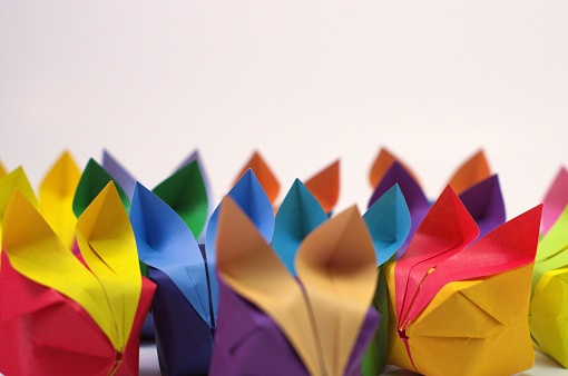 Side view of a large crowd of colorful origami rabbits, facing forwards, against a white backdrop. Focus is on the ears, with a copy space above them.