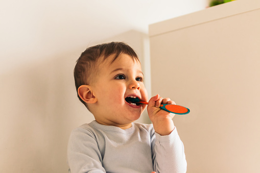 cute baby brushing teeth sitting at home
