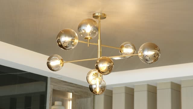 Abstract modern chandelier with round lamps connected by golden metal spokes hanging on suspended ceiling with white plaster skirting boards in modern apartment