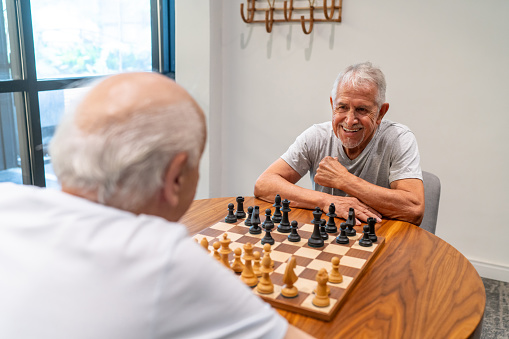 Happy senior man winning at a chess game against a friend at a retirement facility - Lifestyles and leisure concepts