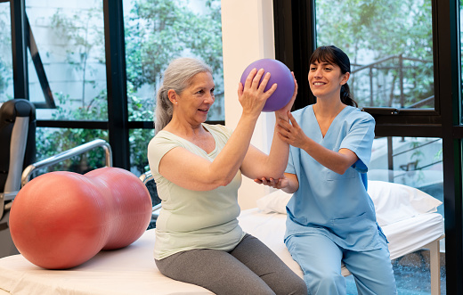 Senior woman working out her arms and shoulders during physical therapy with the help of a female therapist - Healthcare concepts