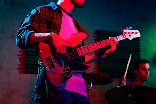 Unrecognizable young man in casual clothes standing in an indoors stage and playing bass in real live concert