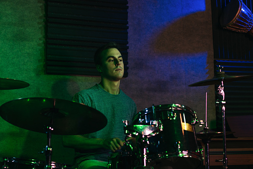 Young musician playing drums on an indoor stage with colored lighting during a live concert