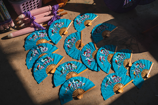 A beautifully displayed pieces of hand-crafted traditional paper fan under the contrasting sunlight in a craftswoman's shop.