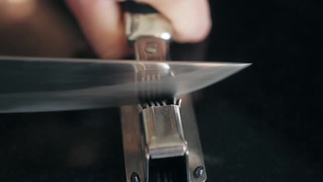 Man Sharpening the knife with a whetstone on a wooden background close up.