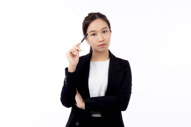 A thoughtful professional young asian woman holding a pen to her face, contemplating, against isolated white background, professional businesswoman pondering with pen, business concept. stock photo