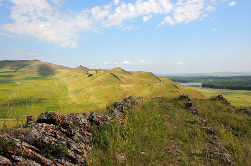 Rocky formations run in parallel rows along the top of a high mountain overlooking a beautiful summer valley in the steppe. Mount Uitag, Khakassia, Siberia, Russia.