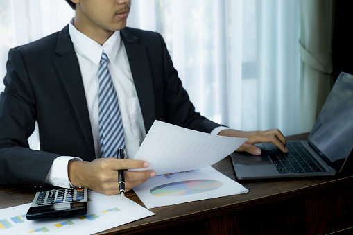 Businessmen bookkeeper hand holding pen and use calculator, laptop analysis the graph for Setting challenging business goals and ready to achieve target at home office.